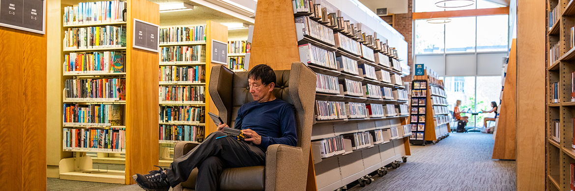 Older patron reading in one of the chairs among all of the bookstacks