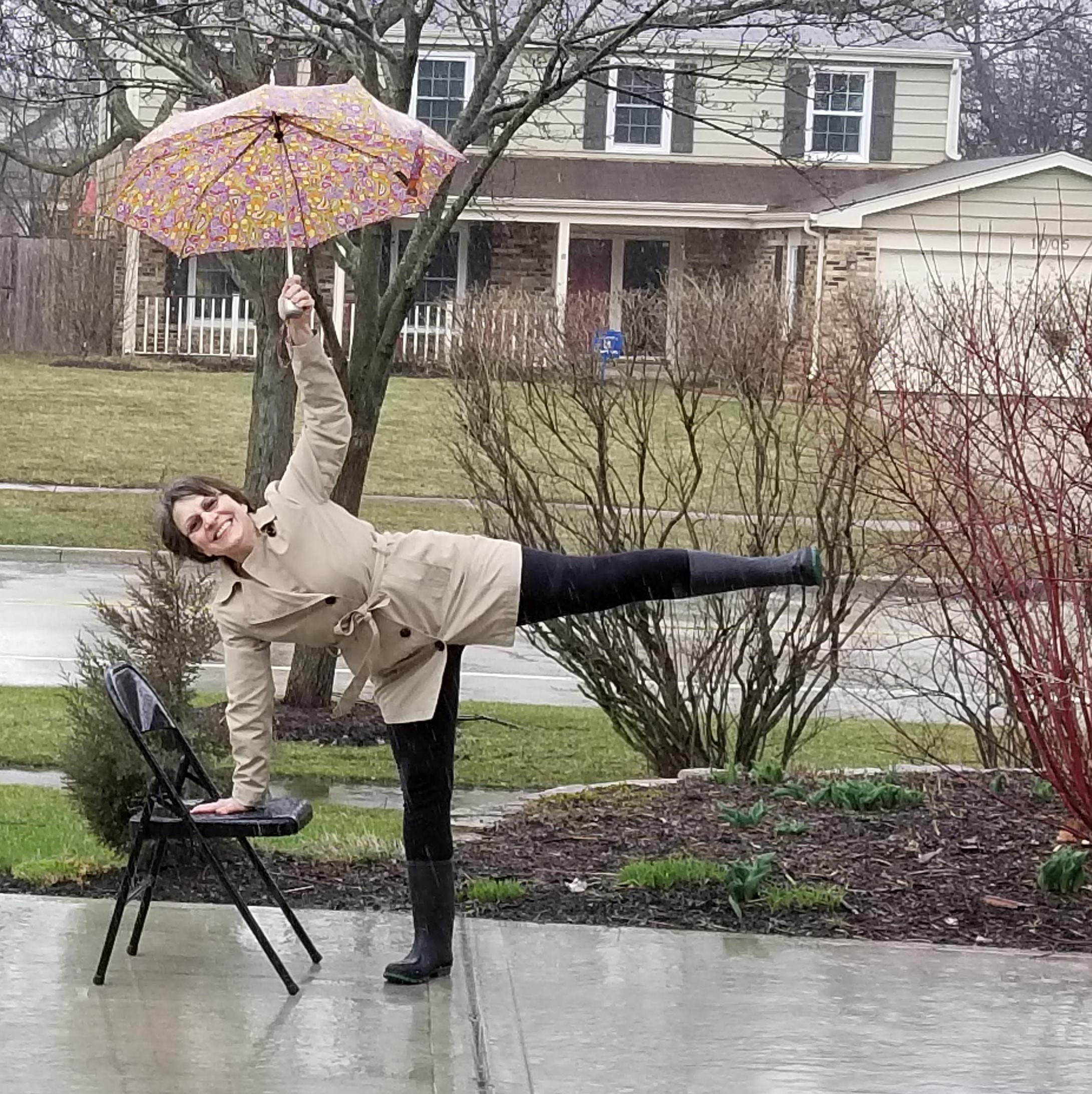 Isabel Raci yoga pose on chair holding umbrella and smiling in the rain