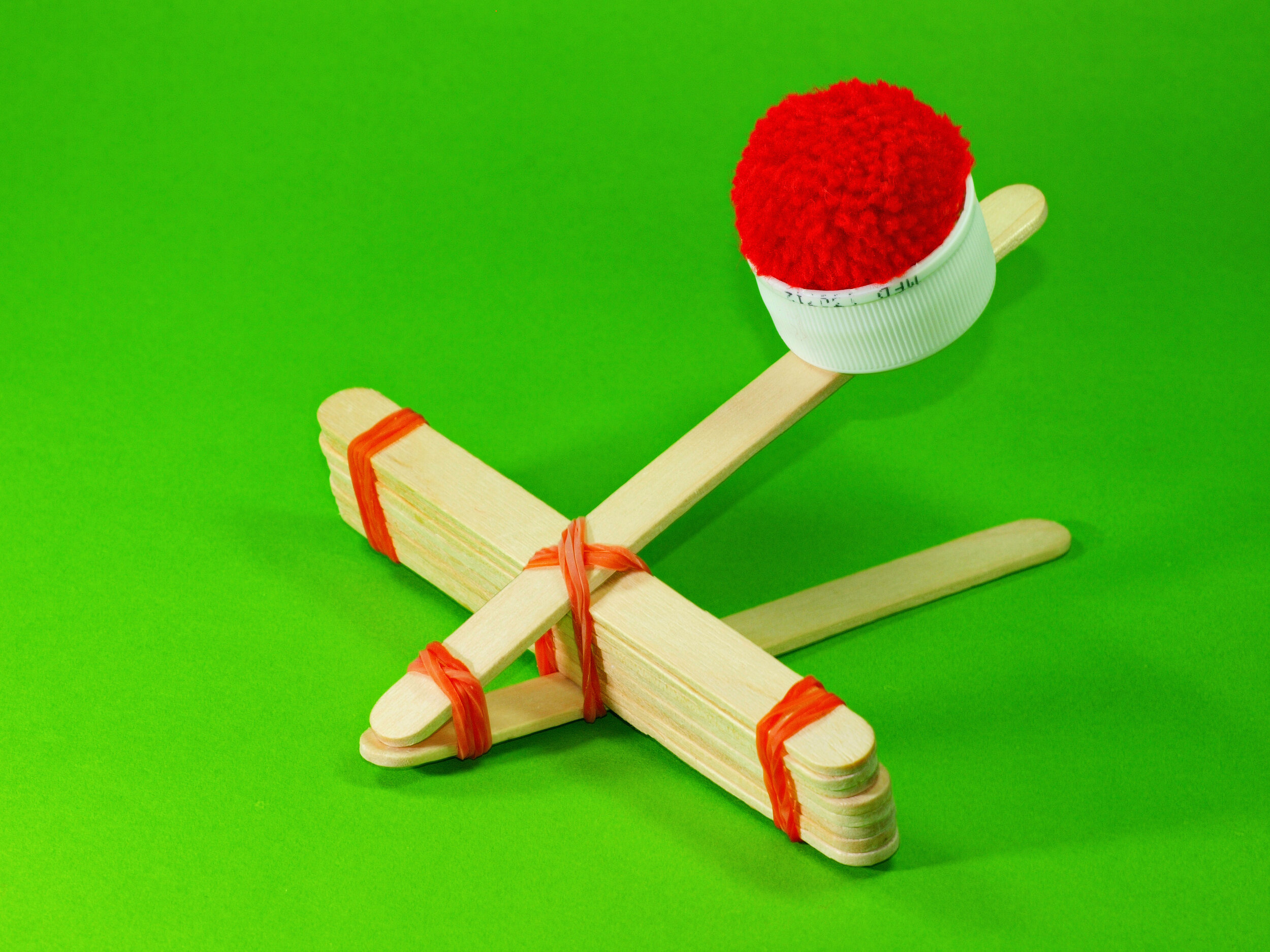 Catapult made out of popsicle sticks with red pom pom ready to be launched.