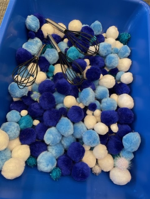 blue and white pom poms in a blue bin with silicone whisks