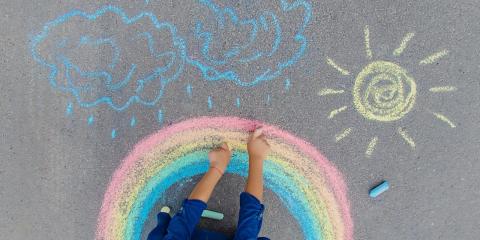 Child drawing a rainbow, sun, and cloud with sidewalk chalk