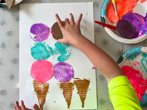 kid using cardboard to stamp paint in the shape of ice cream cones
