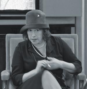 A black and white photo of ElliePresents dressed as Amy McCormick.  She is wearing a 1920's style bucket hat, a dress, and a pearl necklace.
