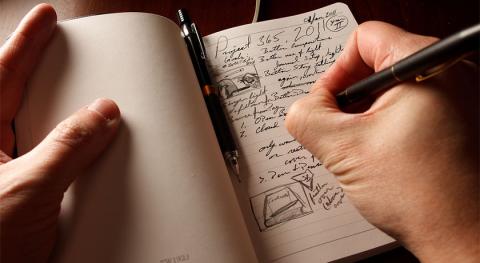 hand with pen writing into journal words and pictures