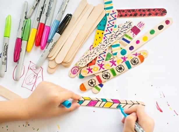 kid coloring popsicle sticks with colorful sharpie markers