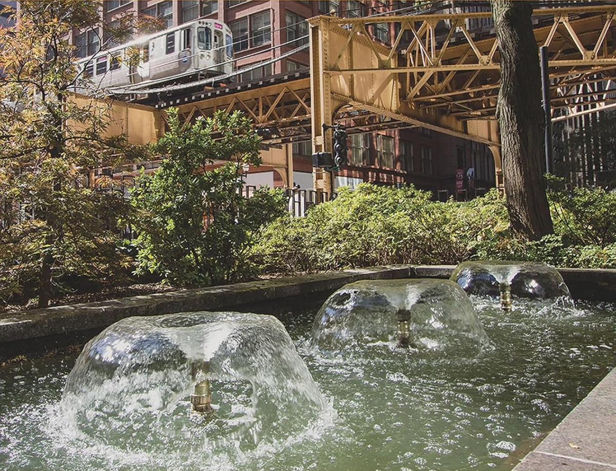 A color image of an outdoor fountain in a garden, with the Chicago "EL" train in the background.