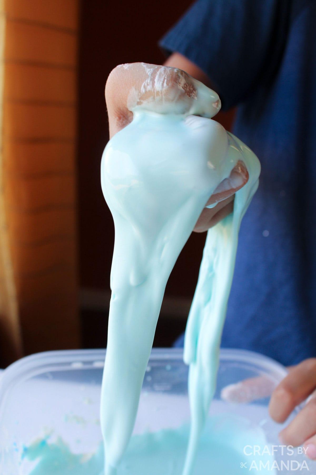 Light blue slime in hand over a bowl with more slime.