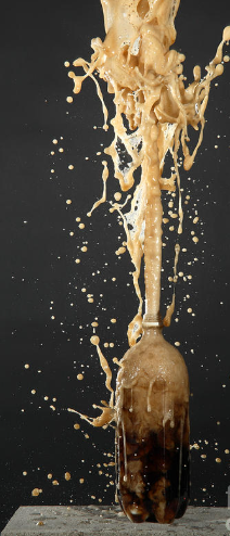 foamy soda bursting in a stream up in the air from bottle below